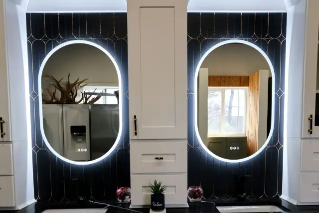 Pair of illuminated oval mirrors above dark vanity displays