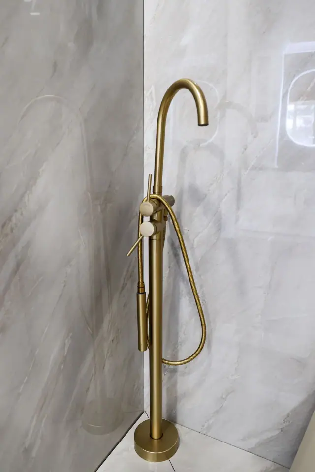 Brass shower wand mounted on a light stone-look wall