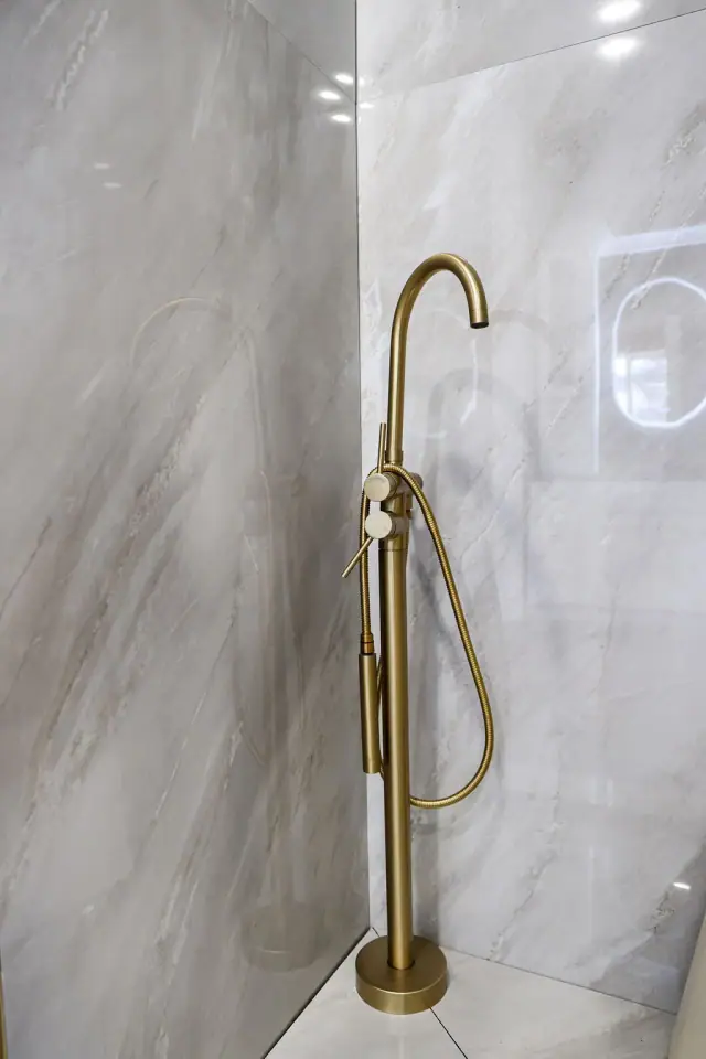 Brass shower fixture on a pale stone-look wall