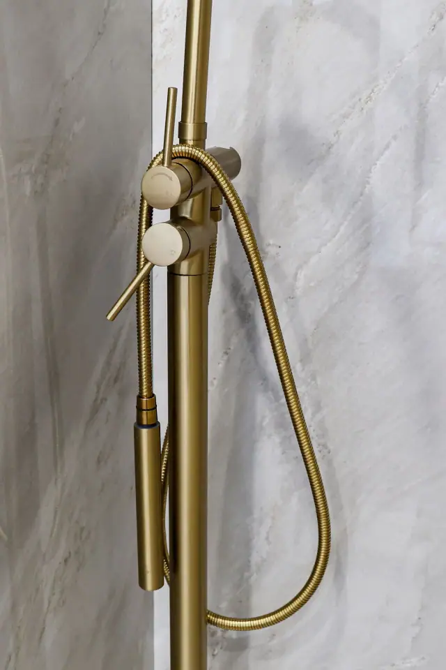 Brass shower wand and hose against pale wall tile