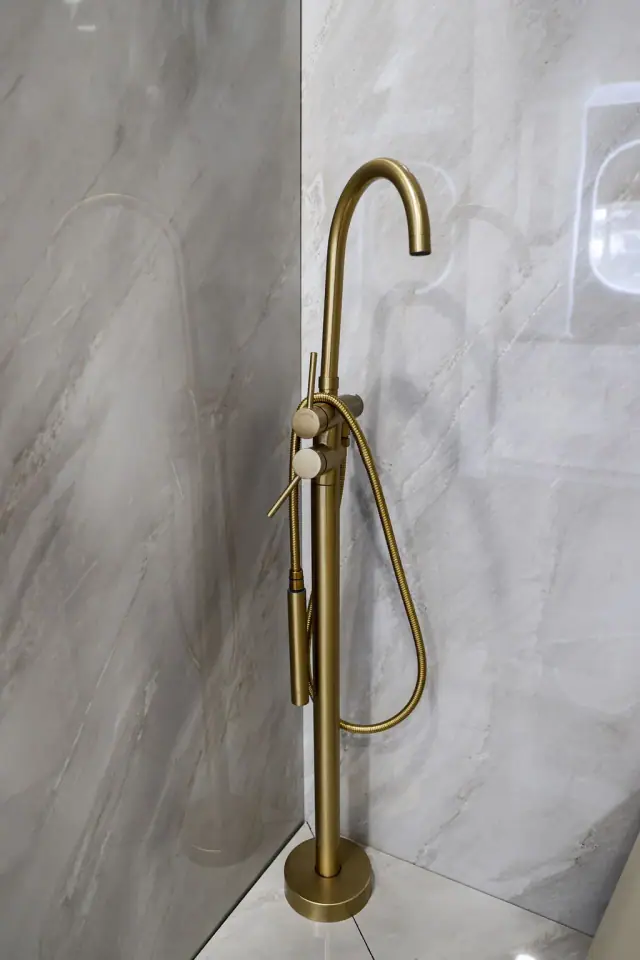 Brass shower fixture displayed on pale stone-look tile
